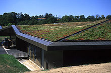 A low building has a roof completely covered with soil and grass. It appears to be built into a hillside