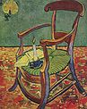 A wooden rocking chair with a couple of opened books set on the green and yellow seat cushion with a lit candle in a holder also on the seat of the chair. On the wall is a burning candle in a holder casting a glowing light.